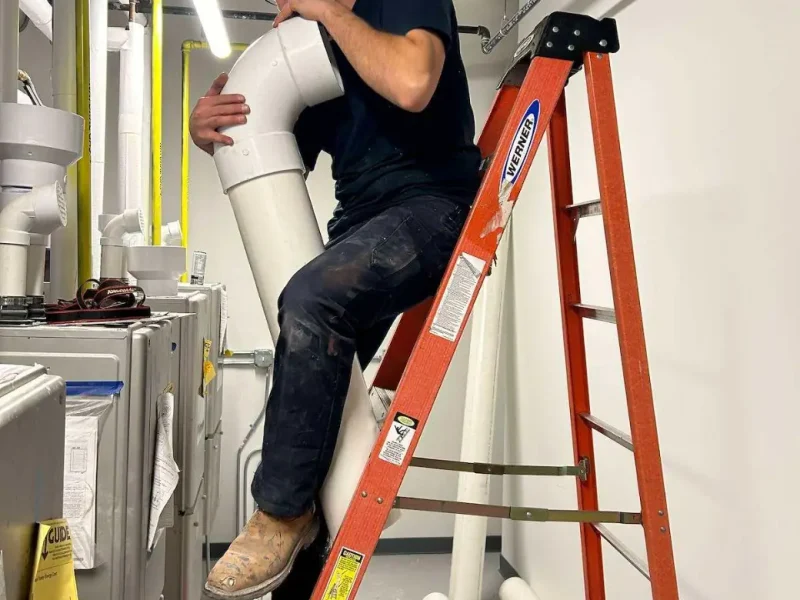 Plumber working on overhead piping in a commercial mechanical room