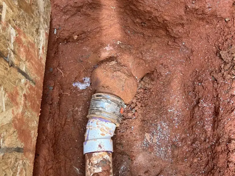 New PVC sewer pipe fitting in a red clay trench