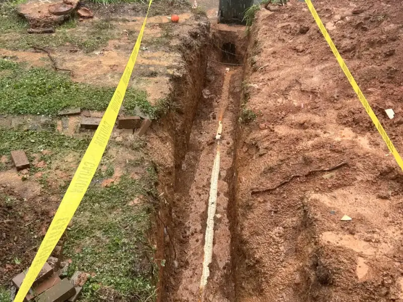 Sewer line trench with new PVC pipe and cleanout, taped off for safety