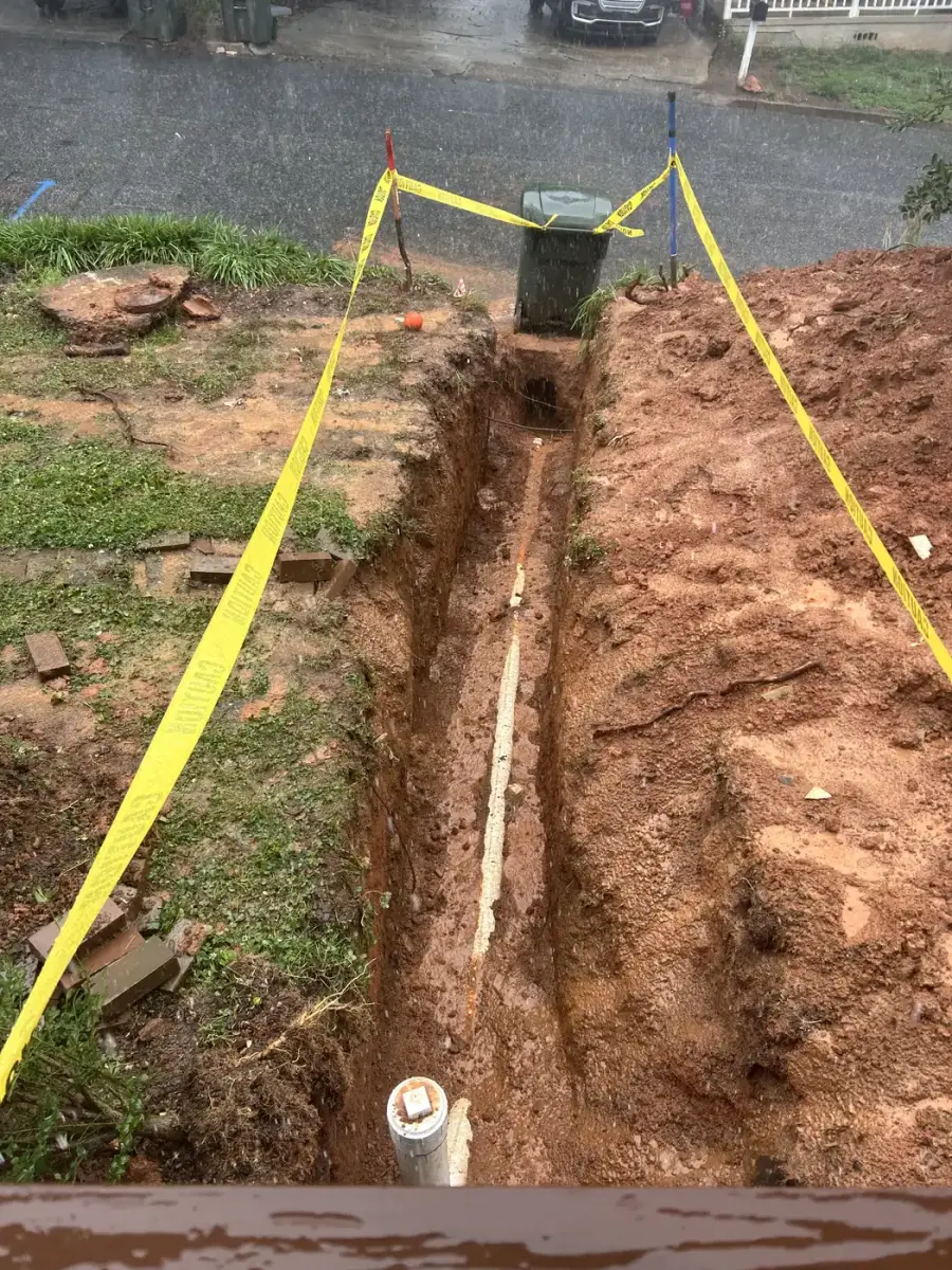 Sewer line trench with new PVC pipe and cleanout, taped off for safety