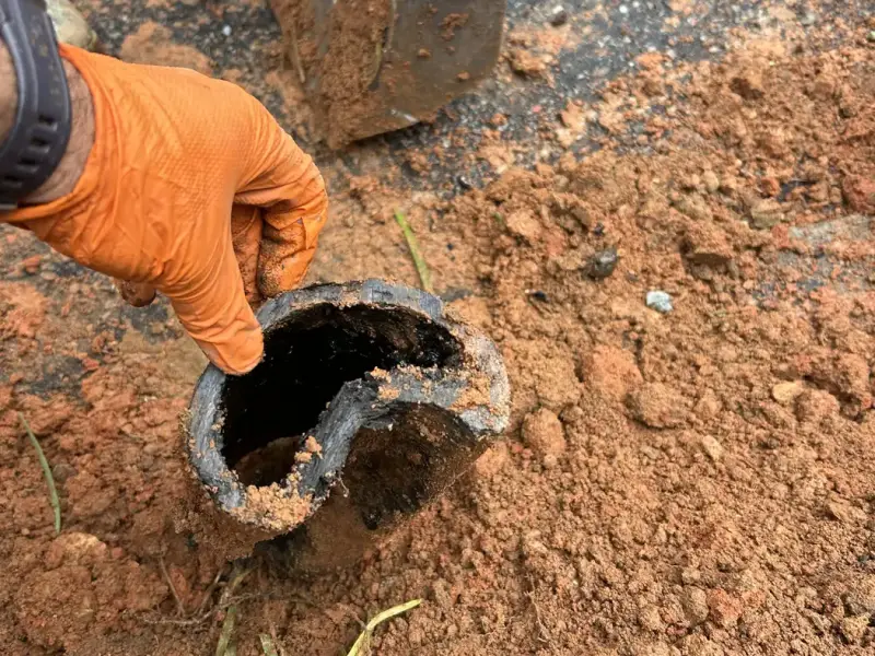 Plumber holding a section of failed sewer pipe removed from the trench